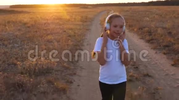 年轻的运动女孩戴着耳机慢跑一个年轻女孩在日落时训练听音乐视频的预览图