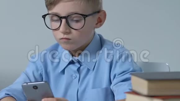可爱的戴眼镜的男孩在课间玩智能手机游戏视频的预览图