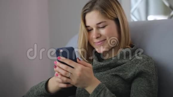 女人在社交网站上浏览智能手机坐在舒适的沙发上视频的预览图