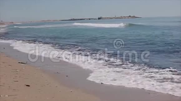 带有泡沫波的桑迪海滨在沙滩上散步的一个穿着短裙子光着脚的漂亮女孩的后景视频的预览图