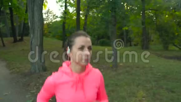 在日落时分一位戴着无线耳机和智能手机的女士在一个秋天的公园视频的预览图