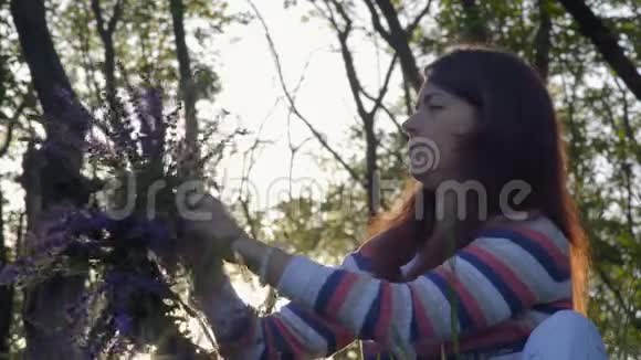 特写镜头美丽的女孩从矢车菊的花中抽出一朵花坐在树林里的早晨视频的预览图