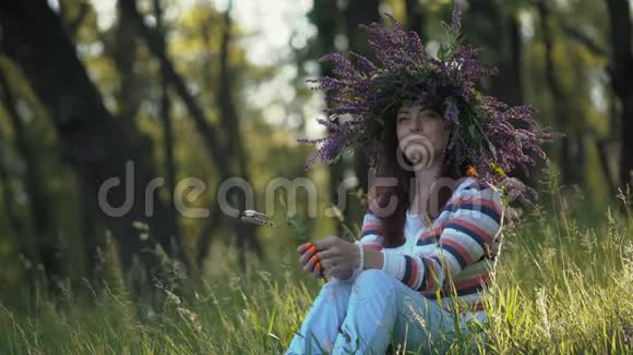 美丽的女孩玉米花的头上长着一朵花在早晨的森林的草地上视频的预览图