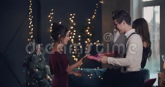 快乐的年轻女子穿着红色时髦的裙子女孩收到生日礼物和新年圣诞节笑声拥抱视频的预览图