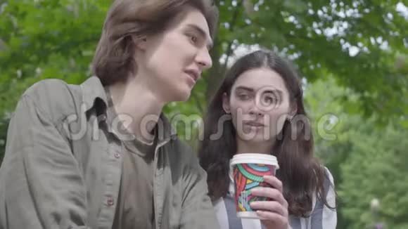 年轻的幸福夫妇穿着休闲服装在公园里一起度过时光约会学生喝咖啡女孩视频的预览图