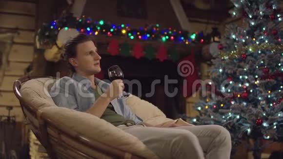 在圣诞夜一个长头发的帅哥坐在装饰好的树旁端着一杯酒视频的预览图
