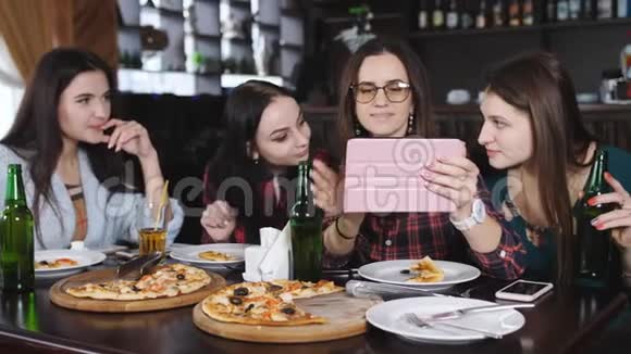 四个女孩在餐厅里在平板上观看照片餐厅里有披萨和啤酒视频的预览图