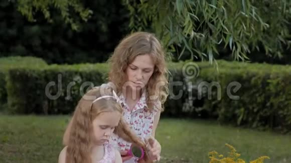 快乐的母亲为女儿梳头日落时分一家人在城市公园野餐视频的预览图