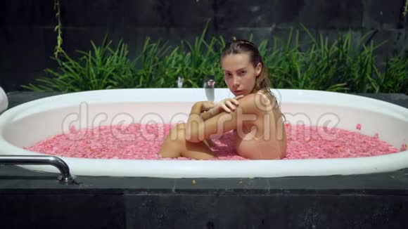侧面特写慢动作女孩坐在充满花瓣的浴缸户外视频的预览图