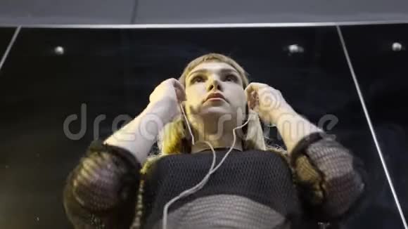 年轻女子戴着小耳机行动带着音乐戴耳机的年轻迷人女性史诗的底部景色视频的预览图