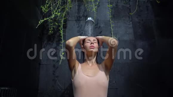 美丽的年轻女性在黑色石墙的室外淋浴下放松视频的预览图