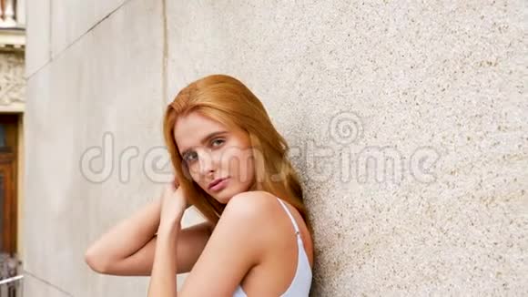 一个美丽而神秘的红发女人靠在墙上看着摄像机视频的预览图