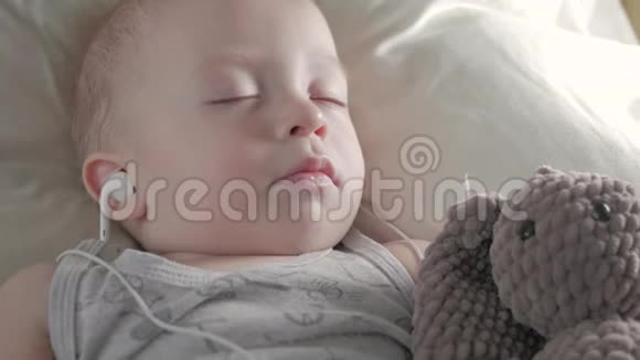 戴着耳机的可爱小男孩和泰迪熊睡在一起视频的预览图