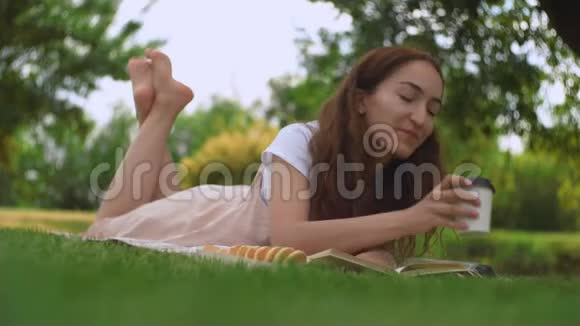 年轻漂亮的女人在夏天公园的草地上喝咖啡视频的预览图