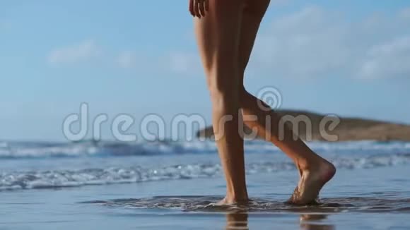 一个女人赤脚在海滩上行走进入海洋的特写镜头慢动作稳定视频的预览图
