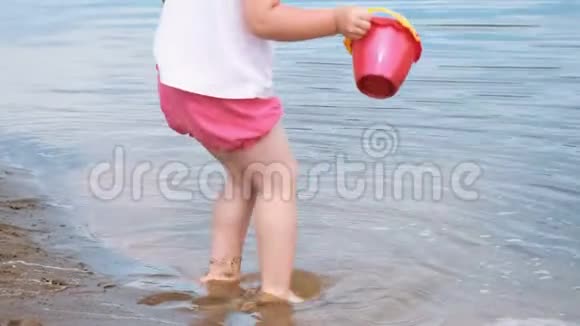 小女孩拿起桶里的水倒进了沙子特写镜头孩子在海滩上玩视频的预览图