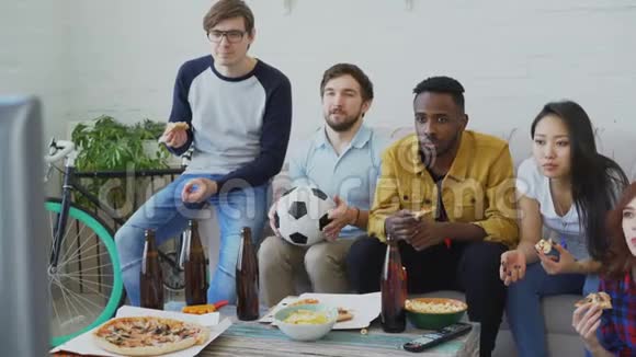 多民族的朋友体育迷在电视上观看足球锦标赛一起吃披萨喝啤酒视频的预览图