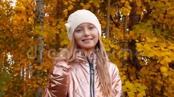 戴着白帽子的可爱微笑女孩站在秋天公园的肖像视频的预览图