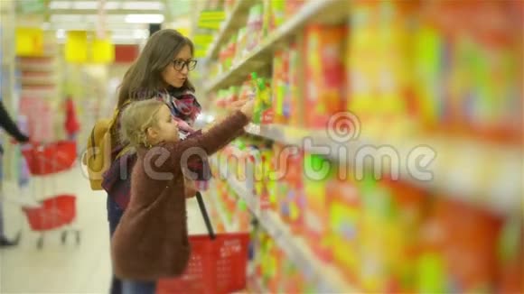 女人和女孩在购物中心选择产品妈妈和女儿把一些东西放在红篮子里后沿着这条路走视频的预览图