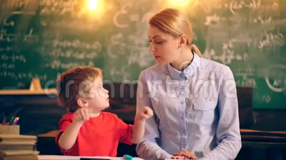 一名教师在学校教室里与一名男孩一起在一块绿色木板的背景下画画概念视频的预览图