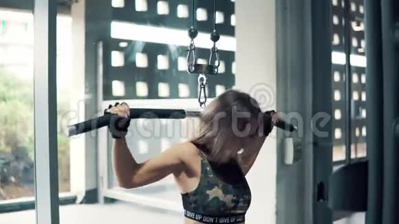 一个年轻健康的女人在健身房用训练机做肩部运动视频的预览图
