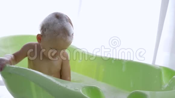 快乐的婴儿变成泡沫坐在明亮的房间里洗澡视频的预览图
