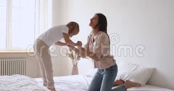 快乐的母亲和孩子牵着手在床上跳跃视频的预览图