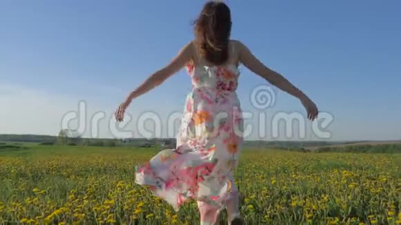 漂亮的女人穿着裙子走在盛开的黄色田野上举起手臂视频的预览图