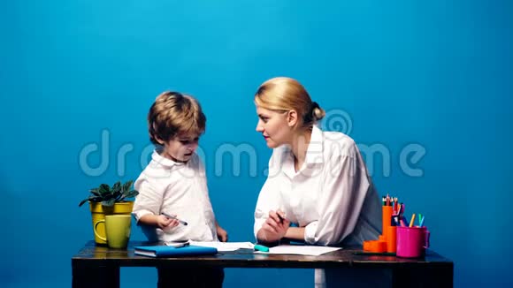 一个穿着白色衬衫的男孩和母亲在蓝色背景下交流和画画视频的预览图