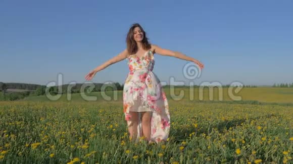 女人站在盛开的黄色田野里穿着连衣裙举起手臂转身视频的预览图