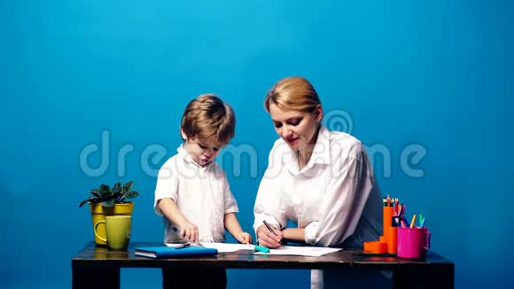 妈妈和儿子一起在蓝色的背景上画画家庭交往观念妈妈和儿子玩有趣的绘画时间视频的预览图