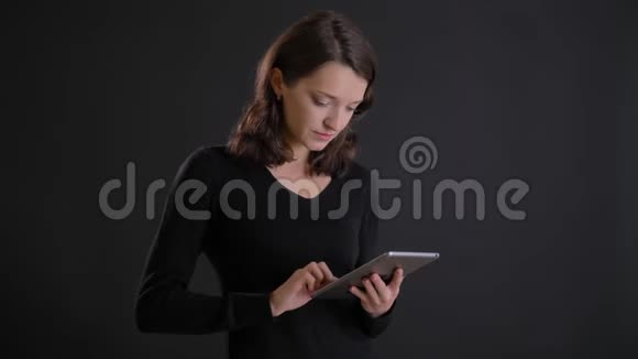 年轻迷人的白种人长发女孩在黑色背景下专心工作平板电脑的肖像视频的预览图