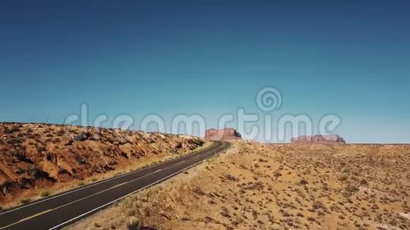 无人机在空旷的沙漠道路上升起揭示了美国阳光灿烂的纪念碑谷令人惊叹的无尽开阔空间视频的预览图