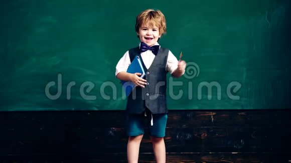 一个手里拿着笔记本和笔的男孩在绿色学校黑板的背景上显示了他的食指学校视频的预览图