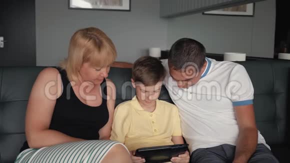 沙发上有平板电脑的幸福家庭有孩子的父母连接到数字平板电脑视频的预览图
