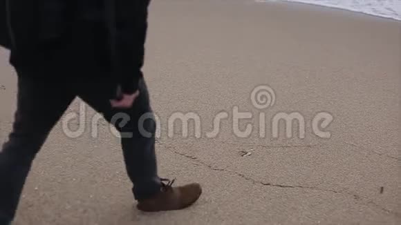 一个人在海滩上捡起一块石头扔进海里的近景视频的预览图