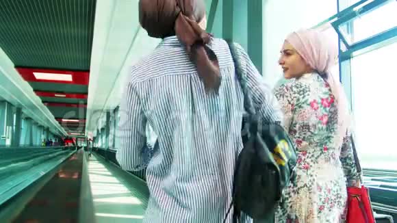 两个穆斯林女孩沿着机场的窗户走着视频的预览图