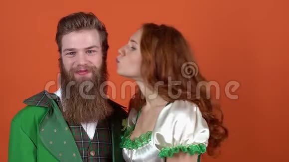 年轻夫妇穿着圣诞服装庆祝圣帕特里克节被隔离在橙色墙上的特写女孩接吻男视频的预览图