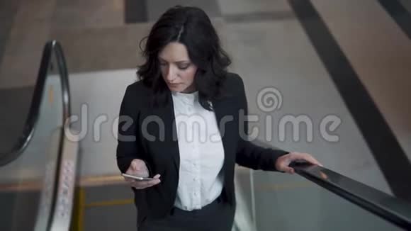 商务女性爬上商务办公楼大厅的自动扶梯视频的预览图