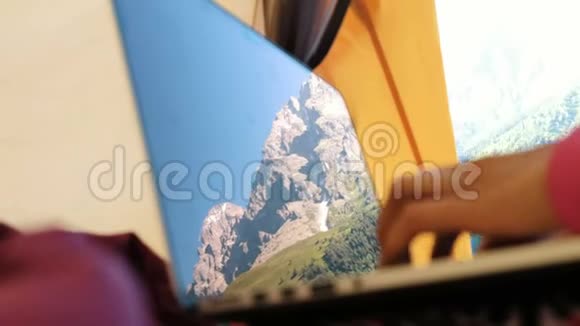 山脉反映在笔记本电脑屏幕上一个女人在旅游帐篷里用电脑在键盘上打特写视频的预览图