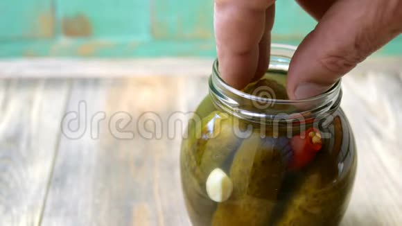 人的手指从木桌上的玻璃罐中取出腌黄瓜或腌黄瓜视频的预览图
