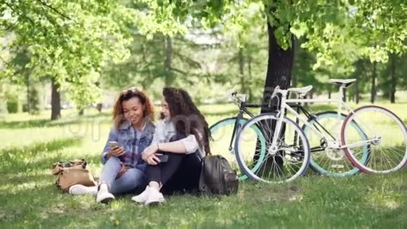 快乐的非裔美国女人正在向她的高加索朋友展示她的智能手机屏幕女孩们正在看它聊天视频的预览图