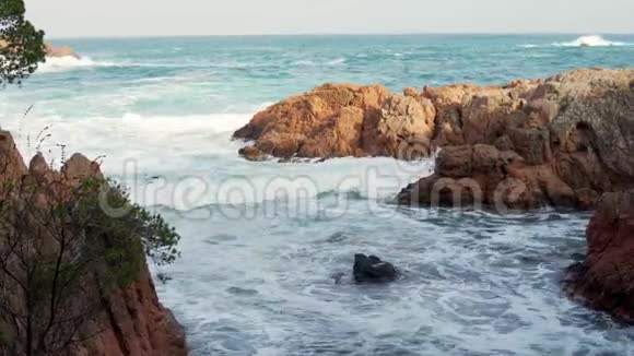 阳光明媚的一天蓝色和祖母绿的大海海浪拍打着岩石视频的预览图