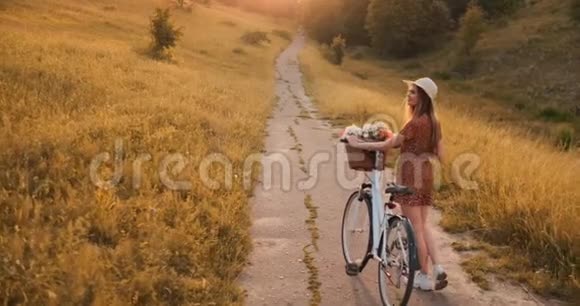 微笑着快乐的女孩穿着连衣裙和帽子骑着复古自行车在公园里看着相机视频的预览图
