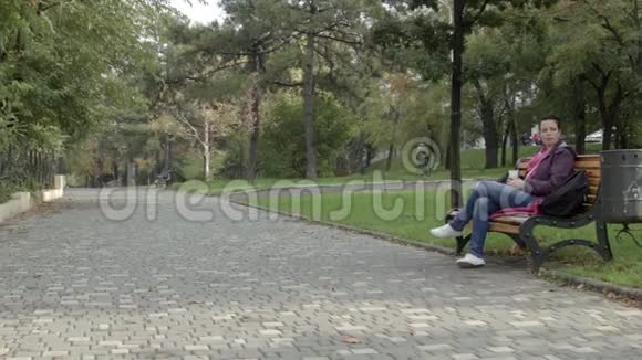 漂亮的女人坐在公园的长凳上喝拿铁她把饮料混合继续喝视频的预览图