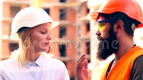施工人员在施工现场进行沟通一个戴着白色头盔的女人和一个戴着橙色胡子的男人交流视频的预览图