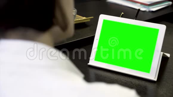 特写一个女人看着一个绿色屏幕的白色平板电脑穿白衬衫的女孩在办公室前工作视频的预览图