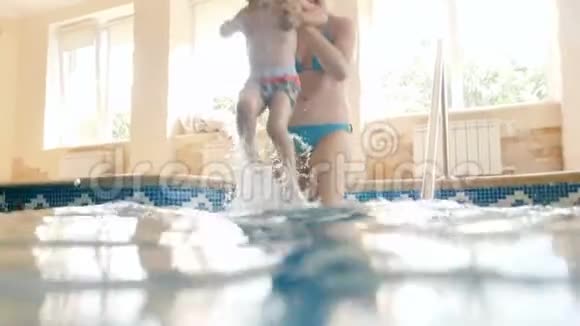 4k视频快乐欢笑的年轻妈妈和快乐蹒跚学步的男孩在室内游泳池走下楼梯视频的预览图