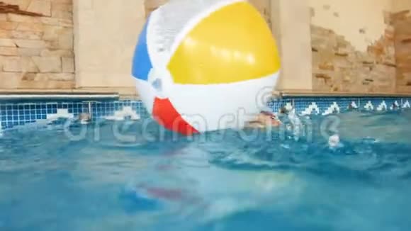 4k镜头快乐微笑的小男孩在游泳池玩充气彩色沙滩球视频的预览图