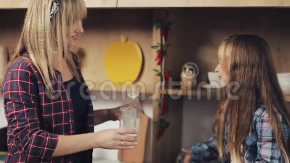 厨房里的幸福家庭妈妈把牛奶倒进她女儿的杯子里钙早餐健康慢动作视频的预览图